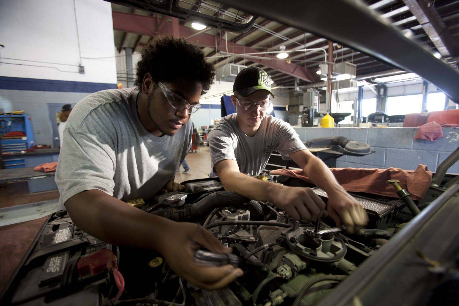 Two students are working on the engine of an automobile. 