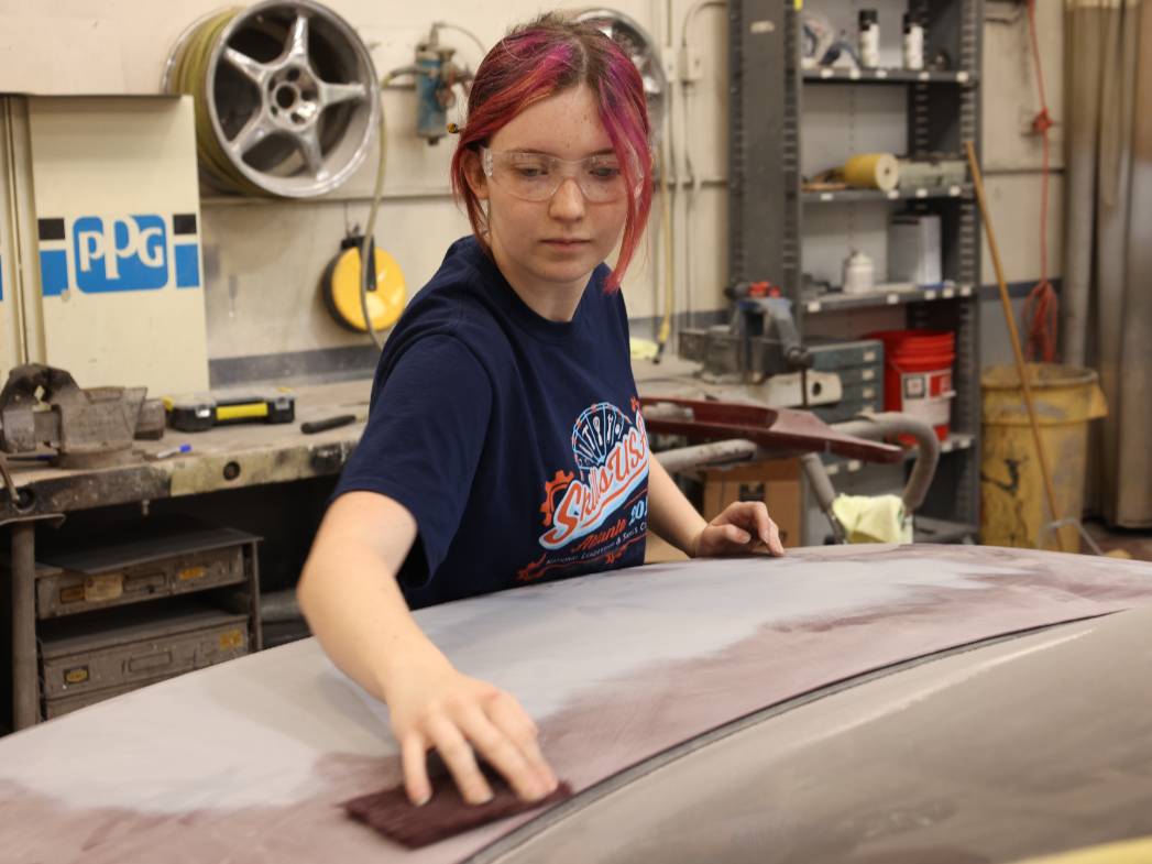 Student is sanding the top of a car to prepare for paint.