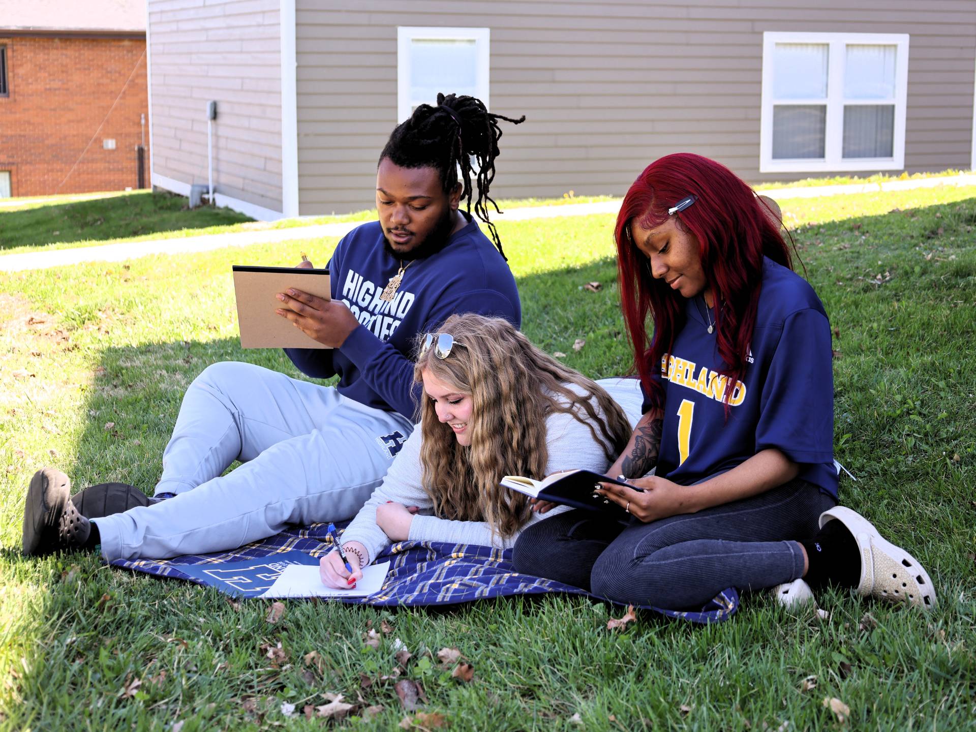 Three students sitting together on the lawn by the dorms