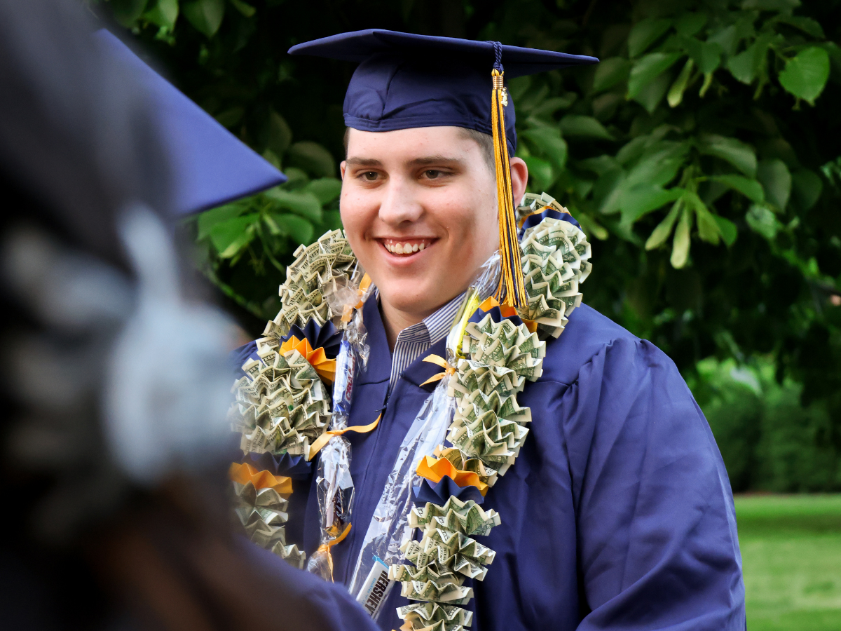Graduate smiles at family. He is wearing a lei.