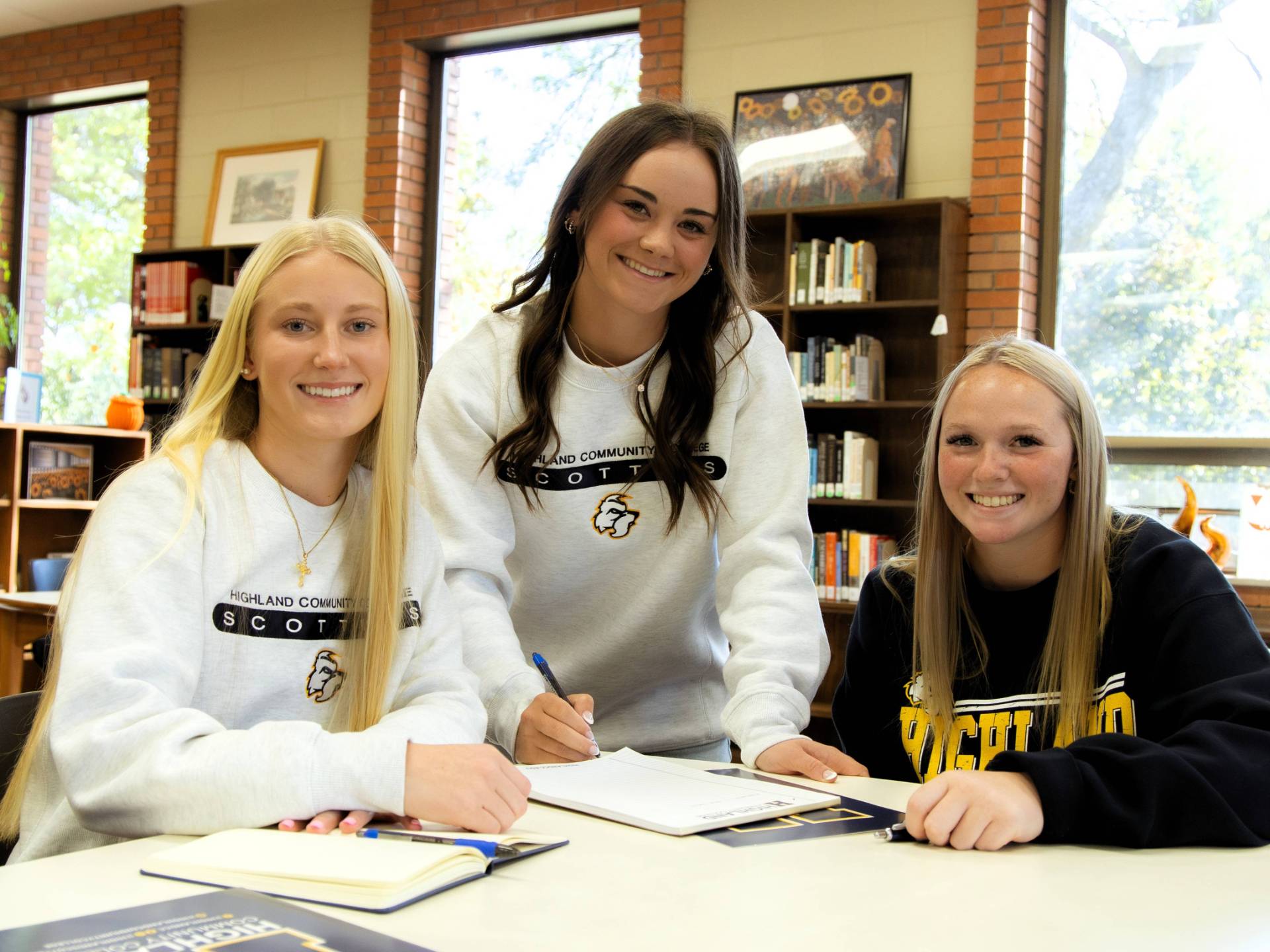 Three students at a table filling out papers, smiling at the camera.